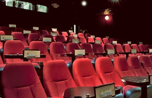 Fauteuils rouges d'un cinéma avec tables pour manger devant