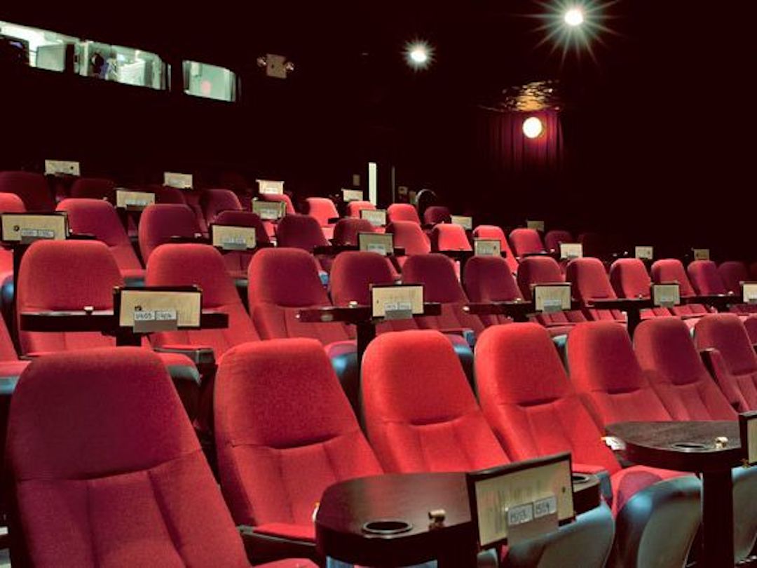 Fauteuils rouges d'un cinéma avec tables pour manger devant